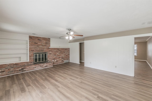 unfurnished living room with a brick fireplace, light hardwood / wood-style floors, built in shelves, and ceiling fan