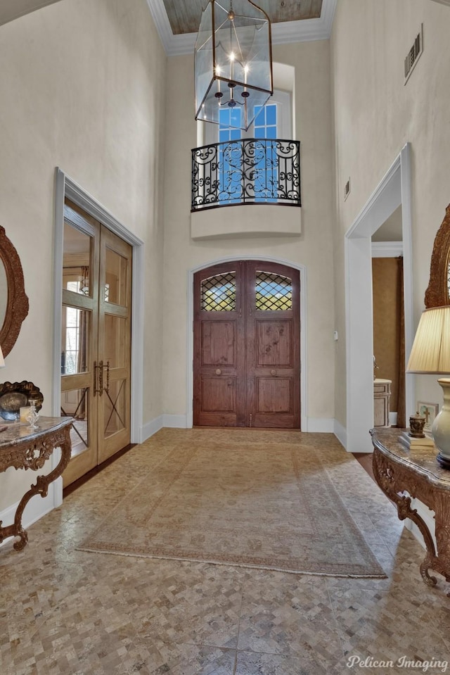 entrance foyer with ornamental molding, a high ceiling, an inviting chandelier, and french doors