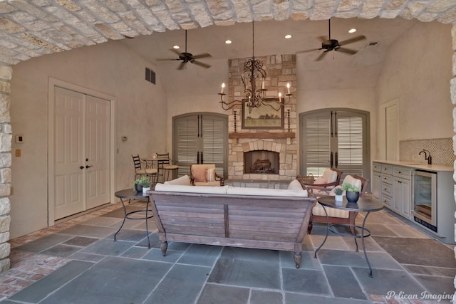 view of patio / terrace with ceiling fan, area for grilling, sink, an outdoor living space with a fireplace, and wine cooler