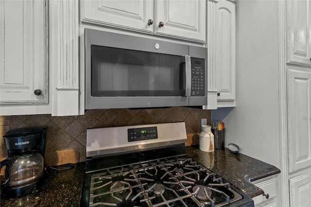 room details featuring dark stone countertops, stainless steel appliances, white cabinets, and backsplash