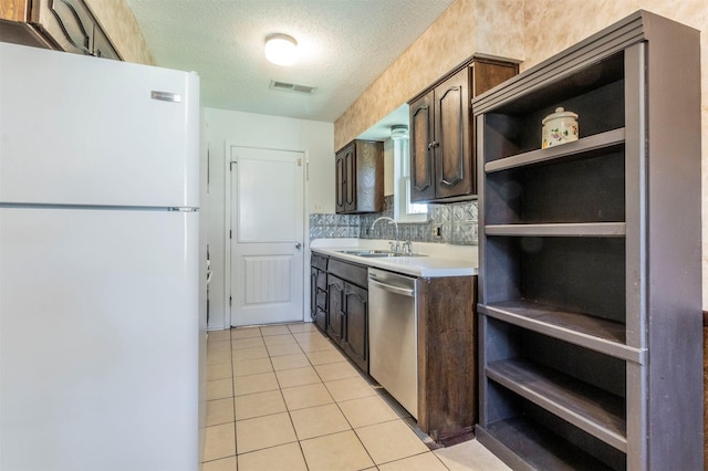 kitchen with sink, stainless steel dishwasher, dark brown cabinets, white fridge, and light tile patterned floors
