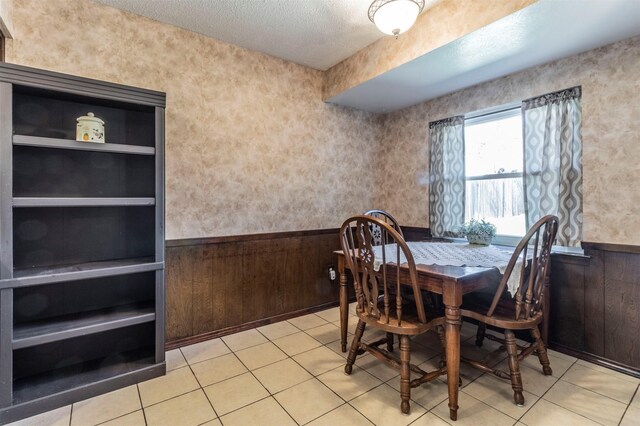 dining area featuring light tile patterned floors, wooden walls, and a textured ceiling