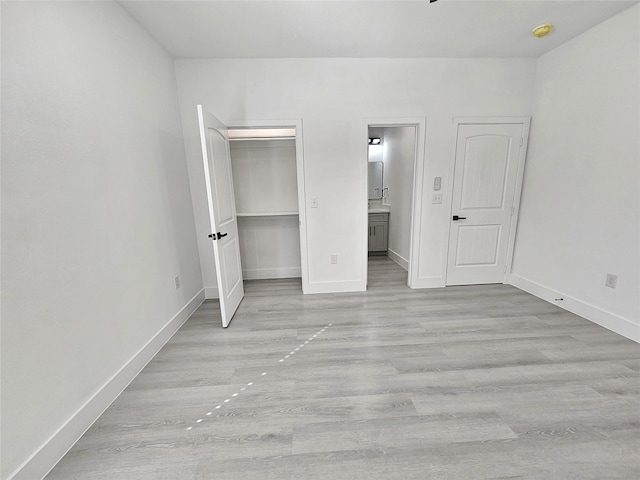 unfurnished bedroom with light wood-type flooring, a closet, a spacious closet, and connected bathroom