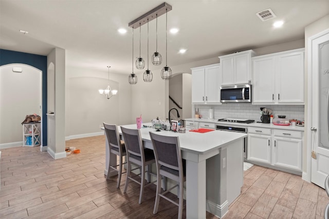 kitchen with white cabinetry, tasteful backsplash, a kitchen island with sink, and decorative light fixtures