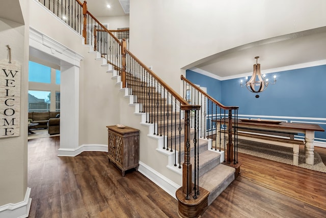 stairs featuring a notable chandelier, wood-type flooring, a high ceiling, and ornamental molding