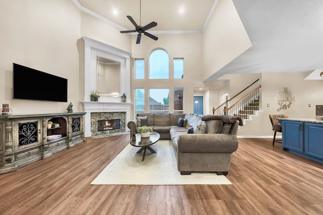 living room featuring light hardwood / wood-style flooring, a stone fireplace, a towering ceiling, ceiling fan, and ornamental molding