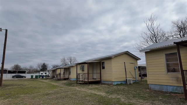 view of side of home featuring metal roof, a yard, and central AC unit