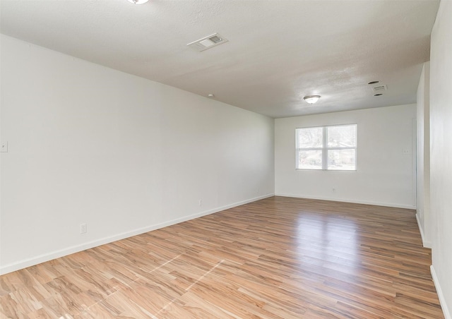 unfurnished room featuring light wood-type flooring, visible vents, a textured ceiling, and baseboards