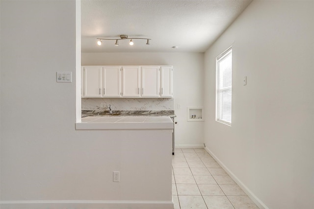 kitchen featuring tile countertops, a textured ceiling, light tile patterned flooring, baseboards, and white cabinets