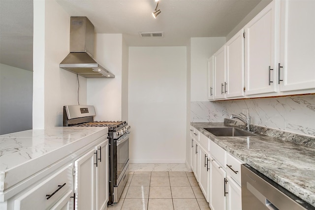 kitchen featuring stainless steel appliances, a sink, visible vents, white cabinetry, and wall chimney range hood