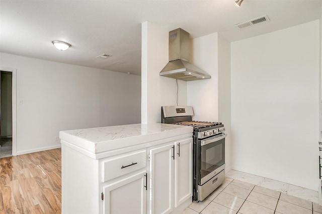 kitchen featuring visible vents, ventilation hood, stainless steel range with gas stovetop, and white cabinets