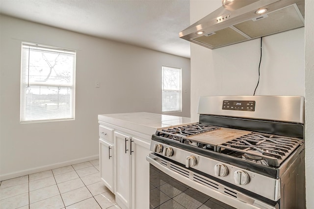 kitchen featuring stainless steel range with gas cooktop, range hood, light tile patterned floors, light countertops, and white cabinetry