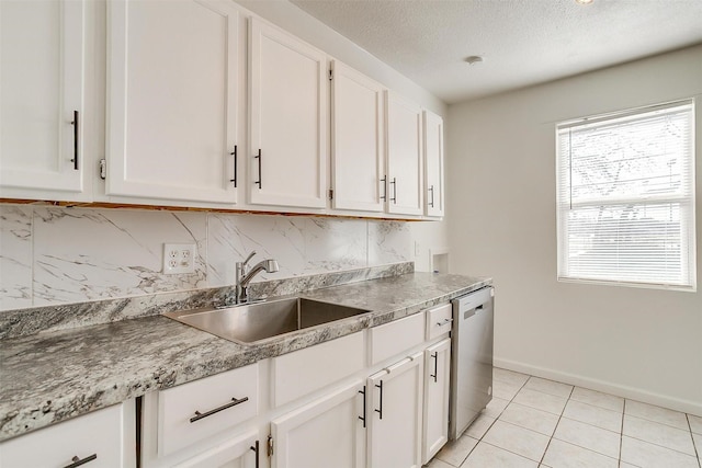 kitchen with light tile patterned floors, decorative backsplash, dishwasher, white cabinets, and a sink