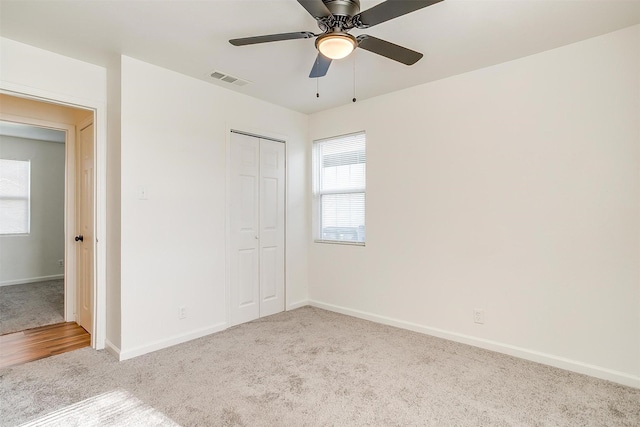 unfurnished bedroom featuring ceiling fan, light colored carpet, visible vents, baseboards, and a closet