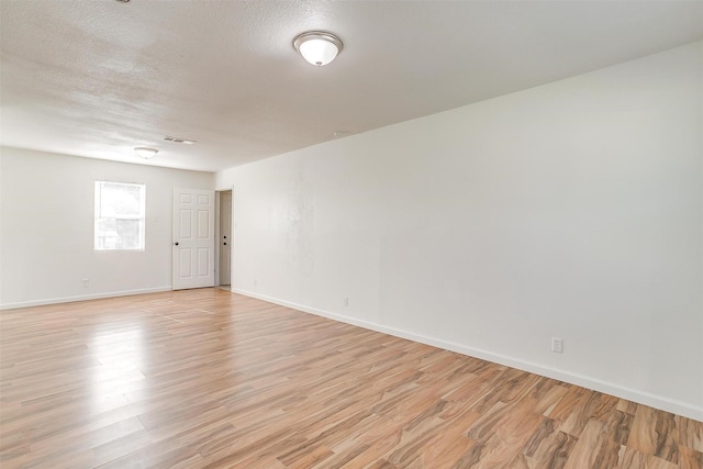 unfurnished room with light wood-style floors, baseboards, visible vents, and a textured ceiling