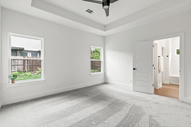 carpeted empty room featuring a raised ceiling, visible vents, ceiling fan, and baseboards