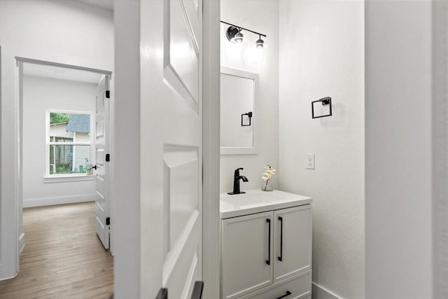 half bathroom with wood finished floors, vanity, and baseboards