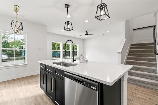 kitchen with an island with sink, decorative light fixtures, dark cabinetry, stainless steel dishwasher, and a sink