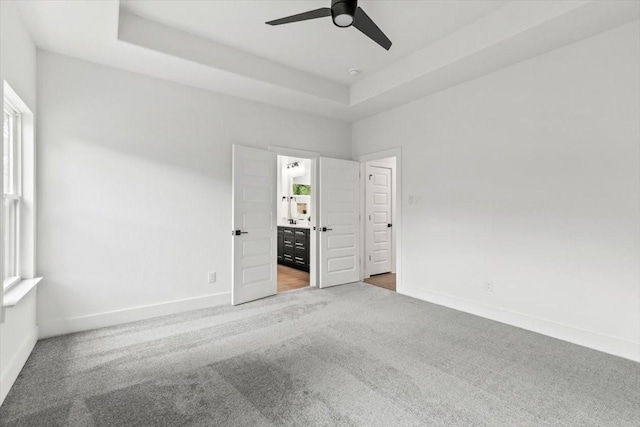 unfurnished bedroom featuring carpet floors, a tray ceiling, multiple windows, and baseboards