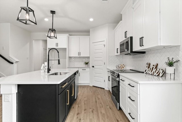 kitchen featuring a kitchen island with sink, stainless steel appliances, white cabinets, light countertops, and pendant lighting