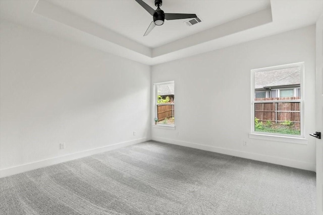 spare room with a tray ceiling, visible vents, and carpet