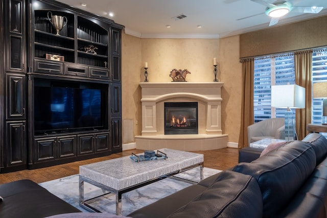 living room with hardwood / wood-style flooring, ornamental molding, a tile fireplace, and ceiling fan