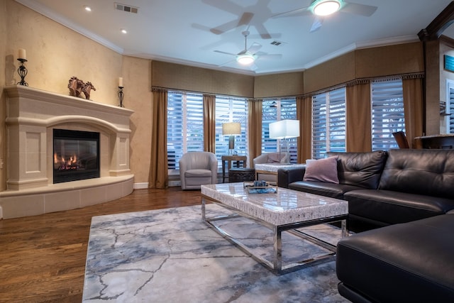 living room with ceiling fan, dark wood-type flooring, crown molding, and a tiled fireplace