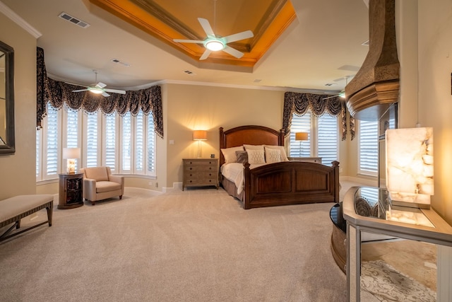 carpeted bedroom featuring a tray ceiling, multiple windows, crown molding, and ceiling fan