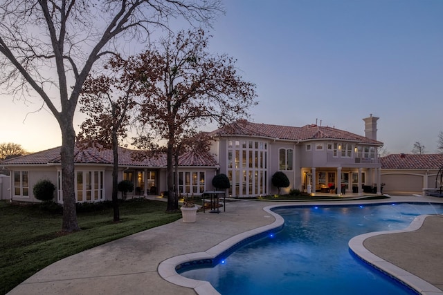 pool at dusk with a patio area and a yard