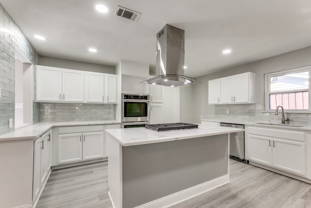 kitchen with appliances with stainless steel finishes, island range hood, sink, and white cabinets