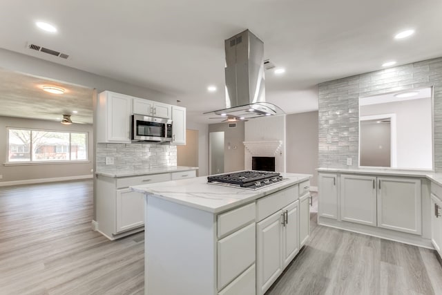 kitchen with appliances with stainless steel finishes, ceiling fan, white cabinets, and island exhaust hood