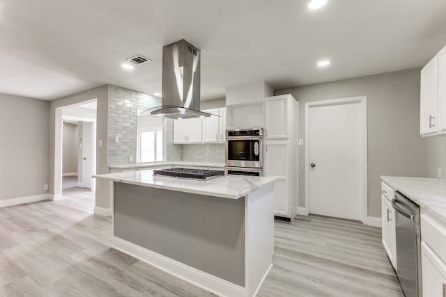 kitchen featuring appliances with stainless steel finishes, island exhaust hood, light stone counters, white cabinetry, and a kitchen island