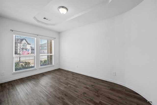 empty room with a raised ceiling and dark wood-type flooring