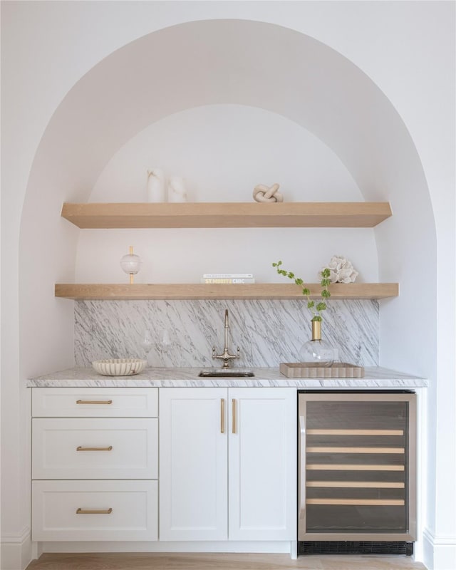 bar featuring sink, white cabinetry, light stone countertops, and wine cooler