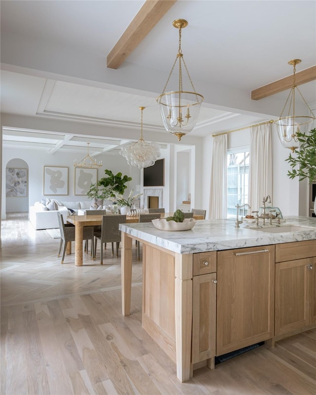 kitchen featuring sink, light stone counters, decorative light fixtures, a kitchen island with sink, and beam ceiling