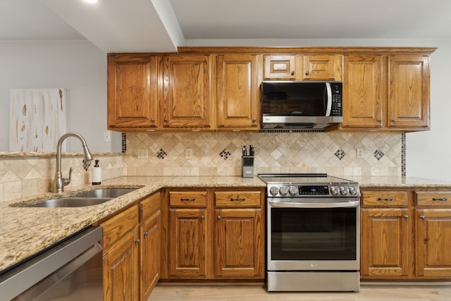 kitchen with decorative backsplash, stainless steel appliances, light stone countertops, and sink