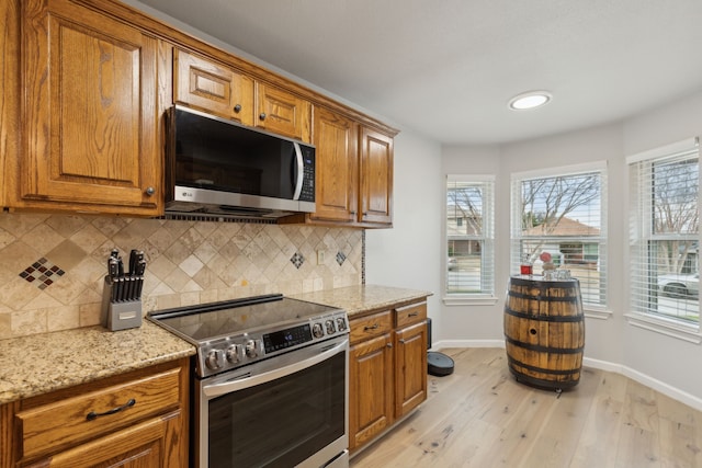 kitchen with light hardwood / wood-style floors, stainless steel appliances, light stone counters, and decorative backsplash