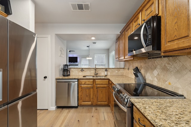 kitchen with stainless steel appliances, decorative light fixtures, light hardwood / wood-style floors, backsplash, and sink