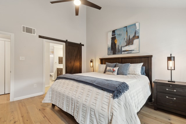 bedroom with high vaulted ceiling, light hardwood / wood-style flooring, ensuite bathroom, and a barn door