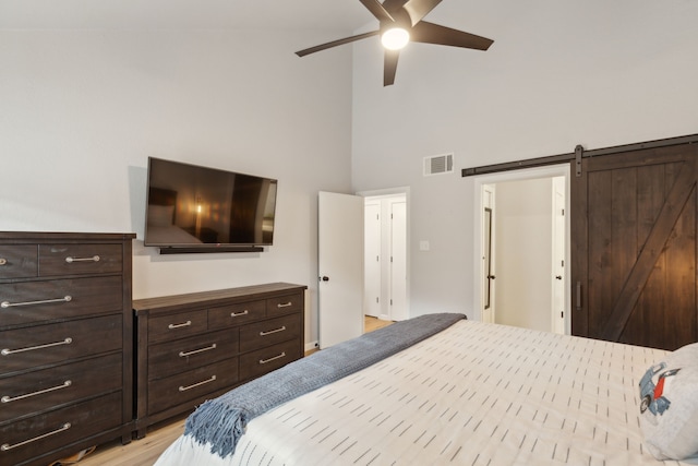 bedroom featuring ceiling fan, a barn door, a towering ceiling, and light hardwood / wood-style flooring