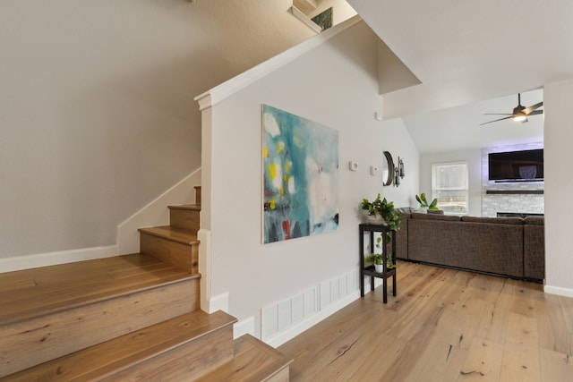 stairway featuring hardwood / wood-style floors, lofted ceiling, ceiling fan, and a fireplace