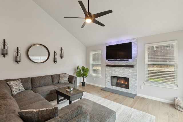 living room featuring high vaulted ceiling, light hardwood / wood-style flooring, ceiling fan, and a stone fireplace