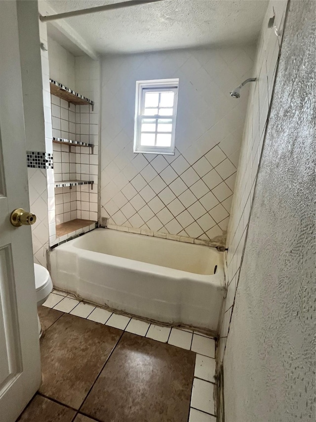 bathroom featuring toilet, tiled shower / bath, a textured ceiling, and tile patterned floors