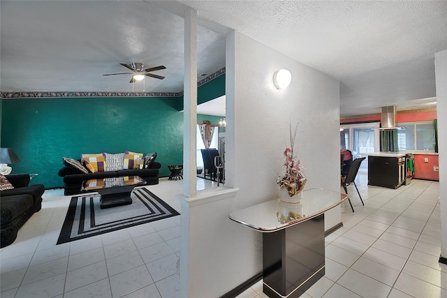 living area featuring a textured ceiling, a textured wall, light tile patterned flooring, and a ceiling fan