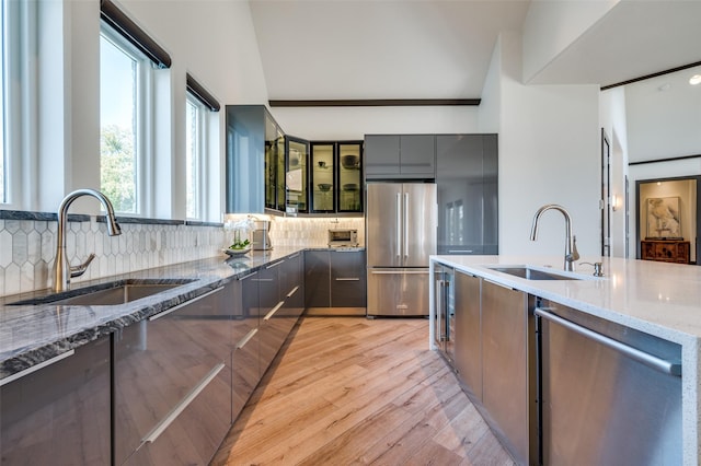 kitchen featuring stainless steel appliances, backsplash, light stone countertops, and sink