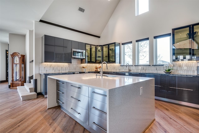 kitchen with a center island with sink, high vaulted ceiling, light hardwood / wood-style floors, and backsplash