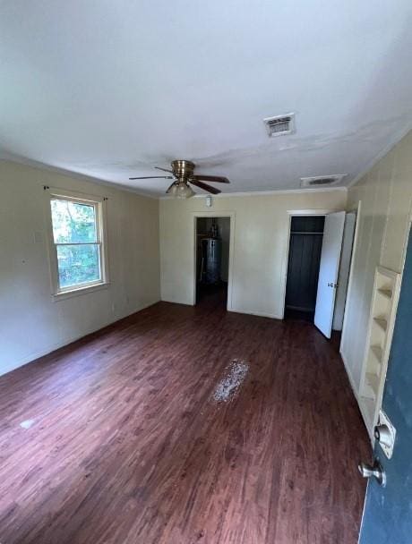 unfurnished bedroom with ornamental molding, ceiling fan, dark wood-type flooring, and multiple closets