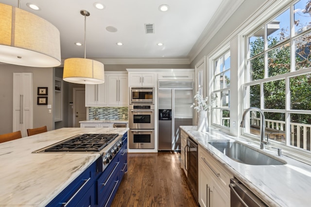 kitchen with white cabinetry, blue cabinetry, built in appliances, sink, and pendant lighting