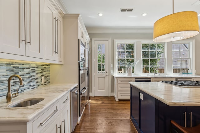 kitchen featuring appliances with stainless steel finishes, sink, light stone counters, pendant lighting, and white cabinetry