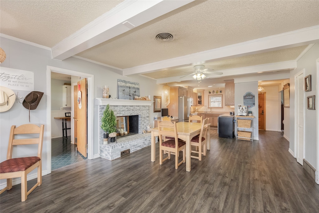 dining space with a textured ceiling, a brick fireplace, beamed ceiling, and crown molding